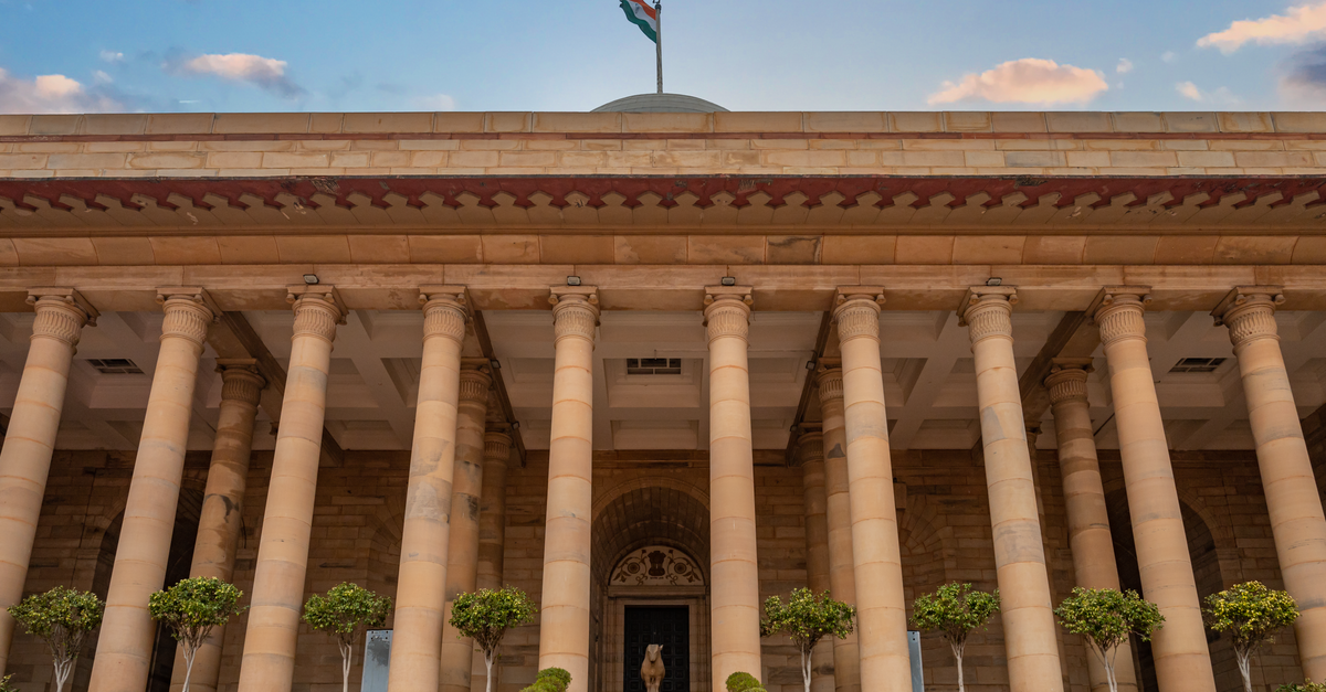 Government building in New Delhi featuring columns and an Indian flag under a vibrant sky.