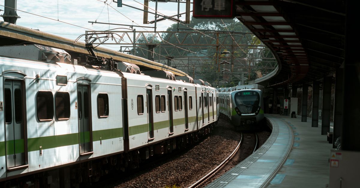 A modern green and white passenger train at an urban station on a bright day.