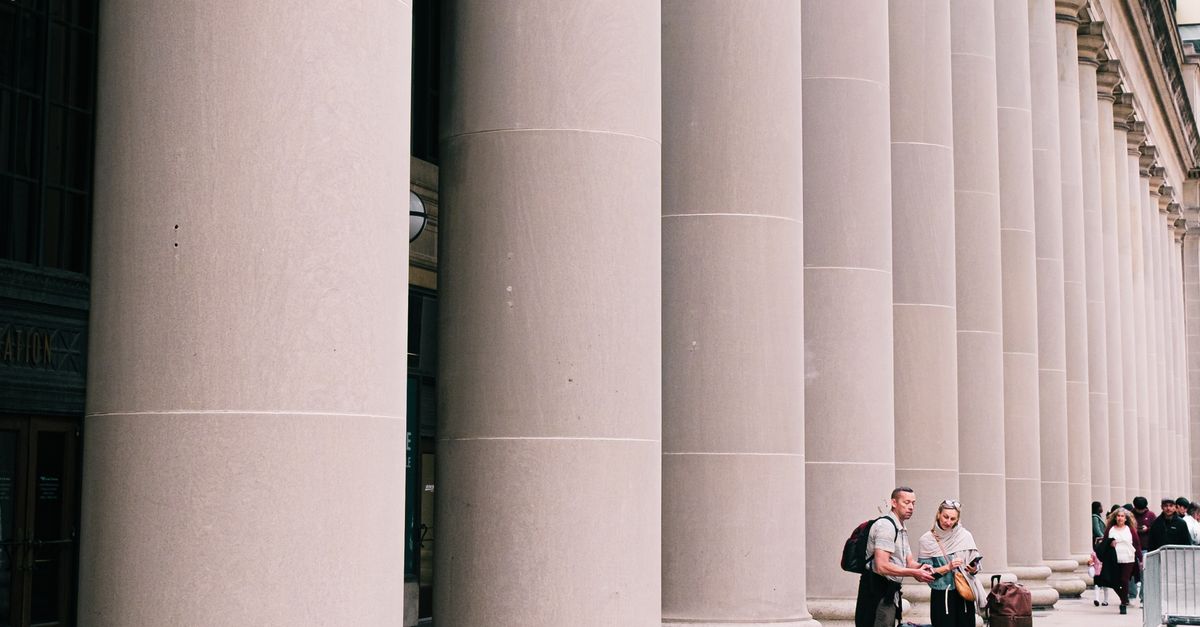 Two travelers stand beside large columns in Chicago, capturing the essence of urban exploration and architectural beauty.