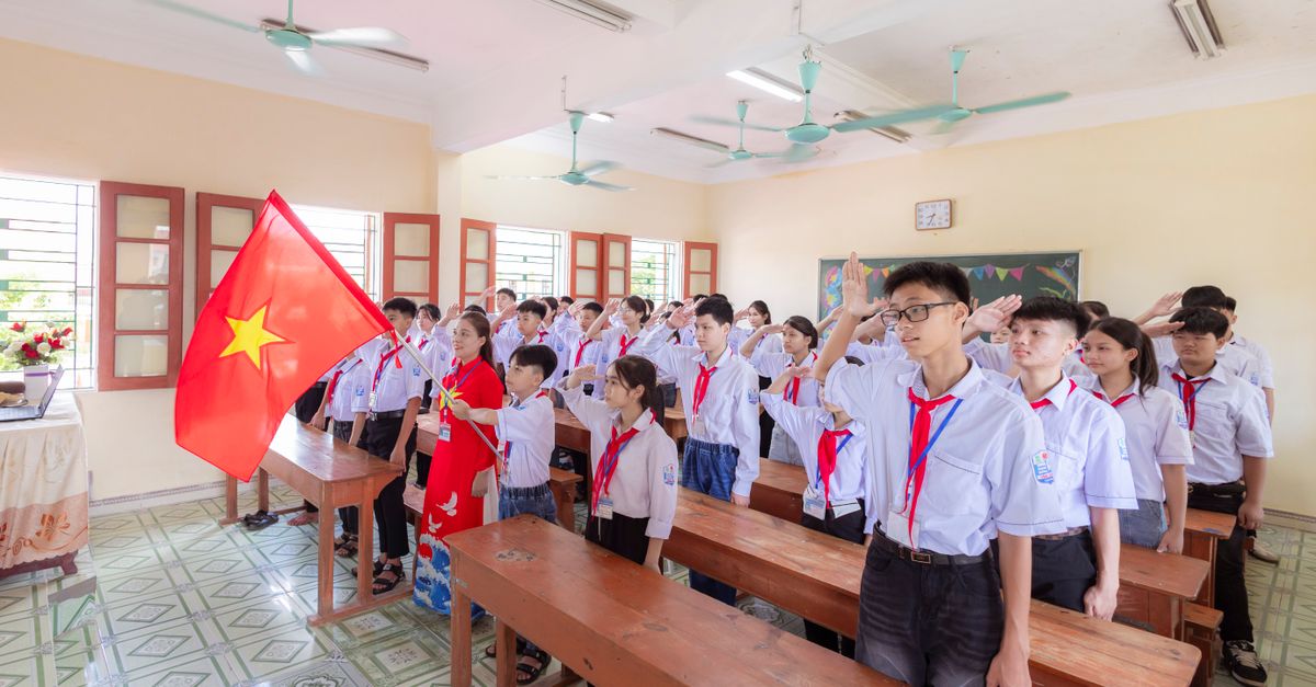 Group of Vietnamese students in uniform saluting the national flag during a classroom ceremony.