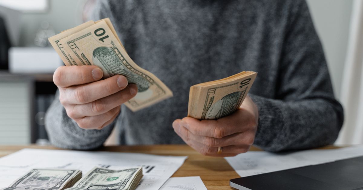 Close-up of person counting cash with a calculator and paperwork on a desk.