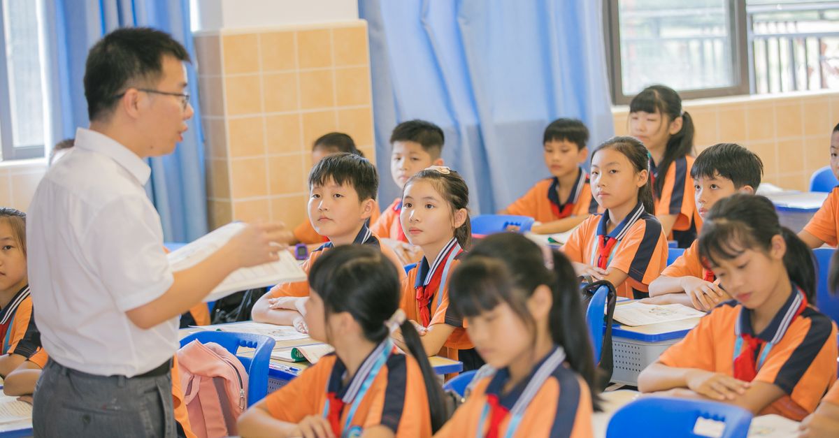 Asian teacher conducting a lesson with attentive students in a bright classroom setting.