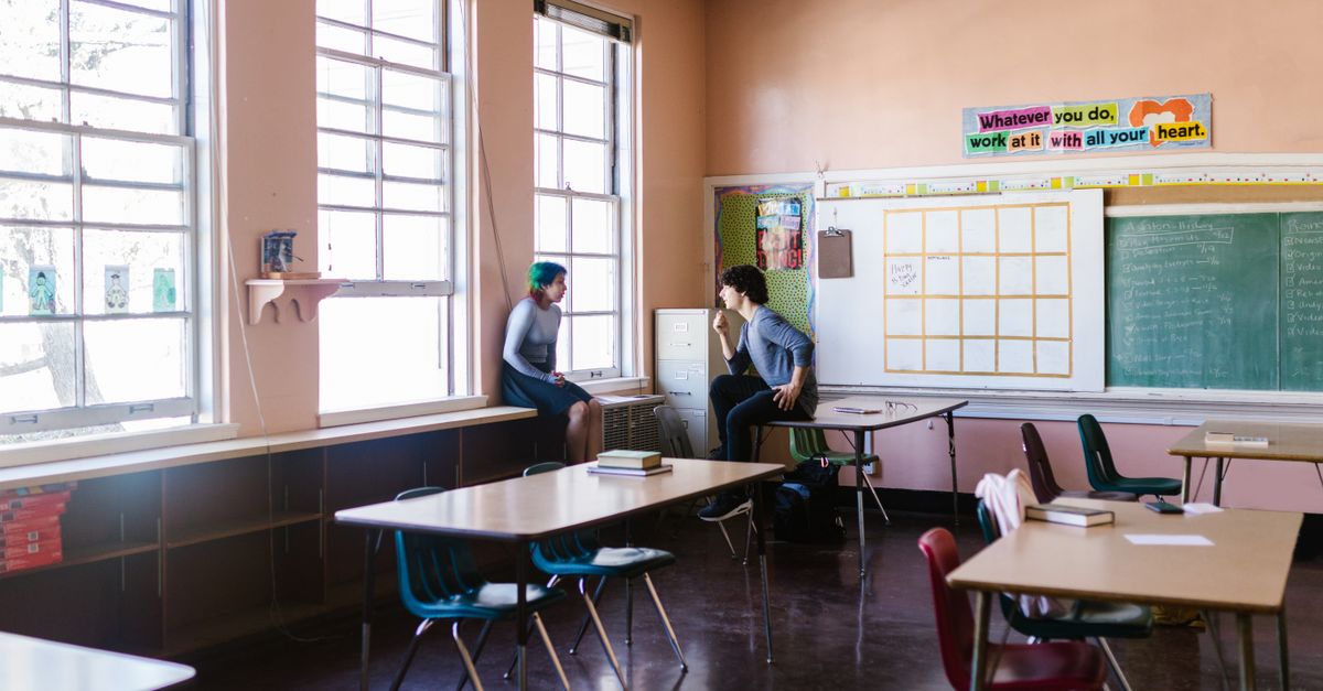 Two adults having a conversation in a bright classroom with large windows.
