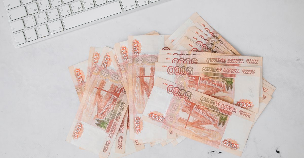 Pile of 5000 ruble banknotes next to a keyboard on a white surface, viewed from above.