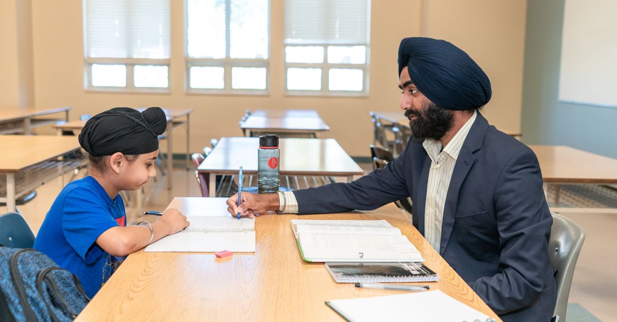 Male teacher helping a young student with studies in a classroom environment.