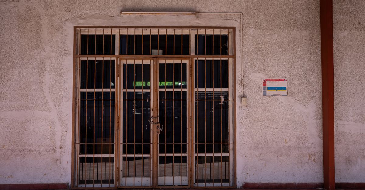A rustic iron gate in a textured wall with a warning sign, captured in bright daylight.