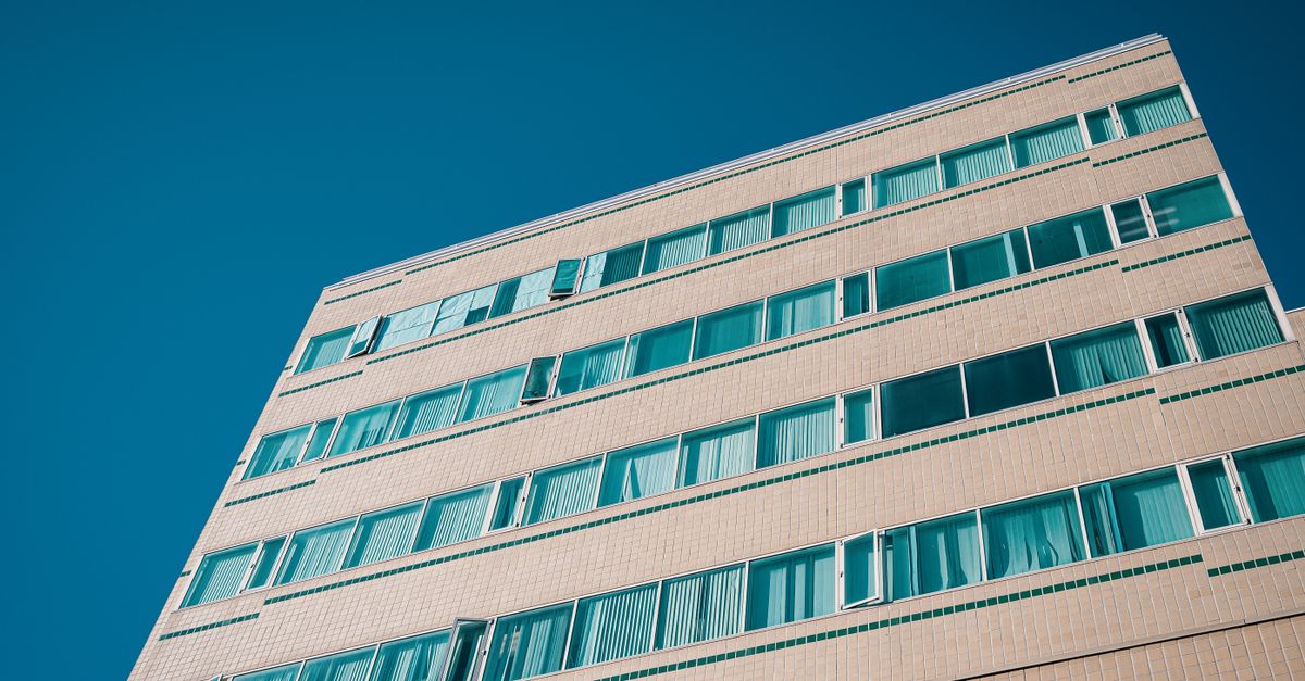 Low angle view of a modern multi-storey building with geometric patterns and blue windows against a clear sky.