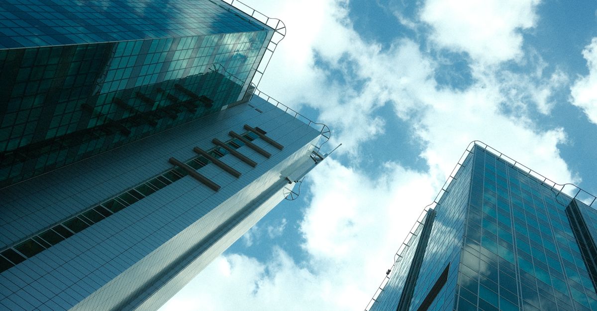 Low angle view of modern glass skyscrapers with clouds reflecting, under a bright blue sky.