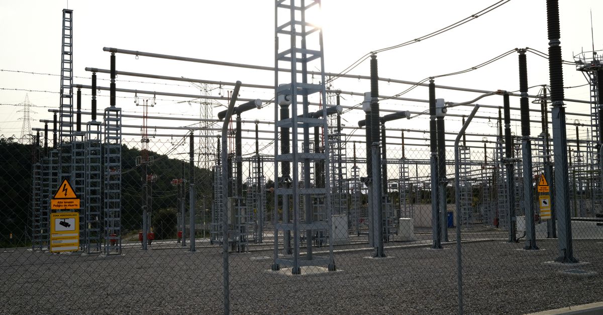 Outdoor electrical power substation with high voltage equipment and safety signs, surrounded by fencing.