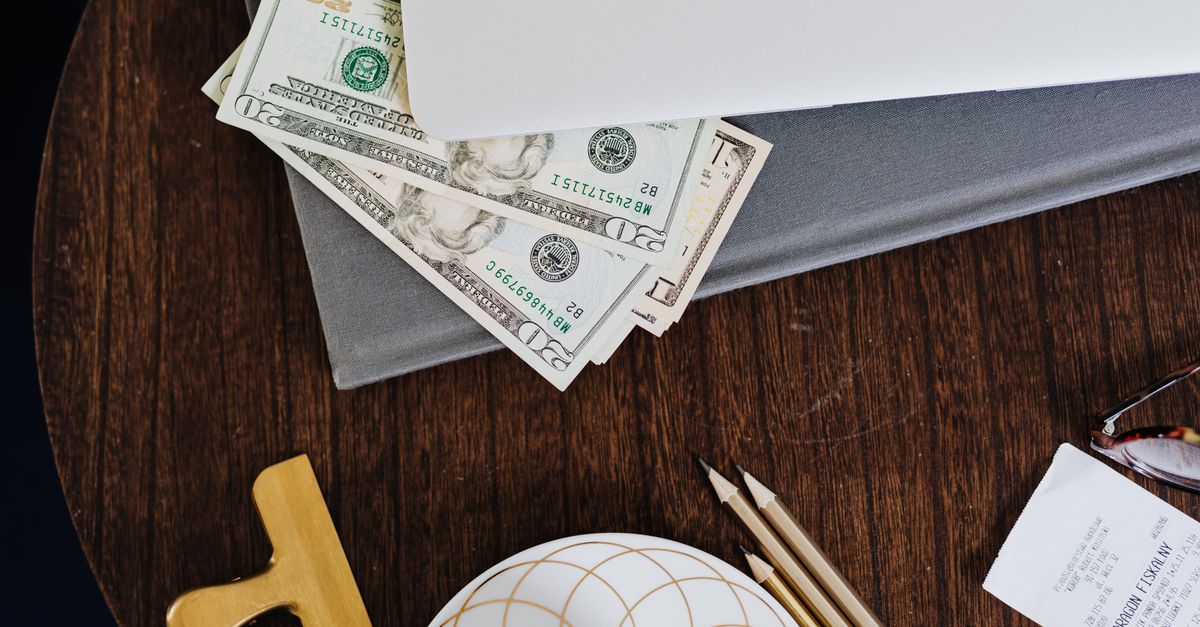 Stylish workspace featuring coffee cup, dollar bills, laptop, and stationery on a wooden table.