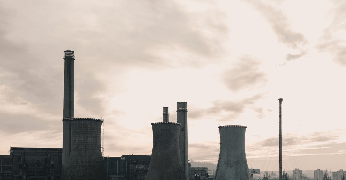 Wide-angle view of an industrial power plant with prominent cooling towers against a cloudy sky.