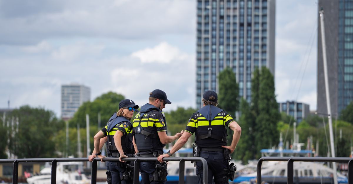 Three police officers stand on a waterfront railing, overseeing a cityscape with high-rise buildings.