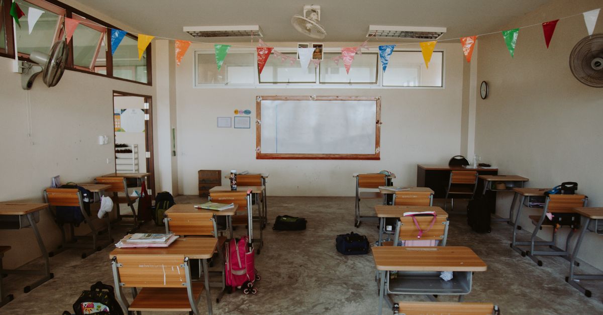 An empty classroom with desks arranged neatly and colorful flags hanging from the ceiling, creating a bright and hopeful atmosphere.
