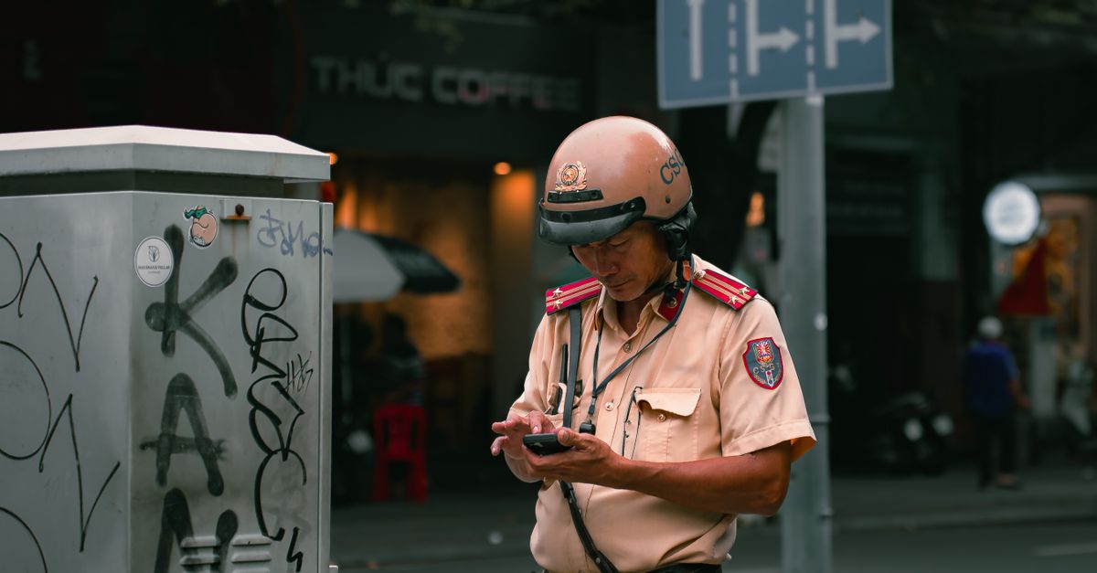 Vietnamese traffic officer checks information on the street. Urban setting with graffiti.