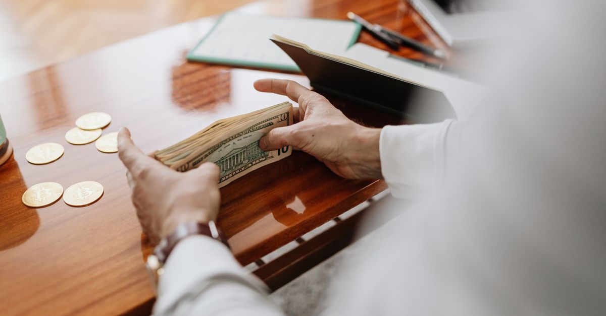 Person counting cash and coins on a wooden table, emphasizing financial tasks.