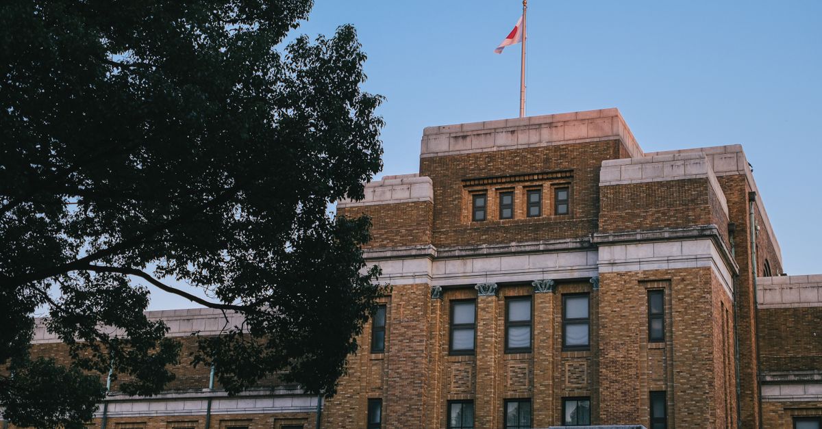 Historic brick building with Canadian flag, tree in foreground. Captured during daylight.