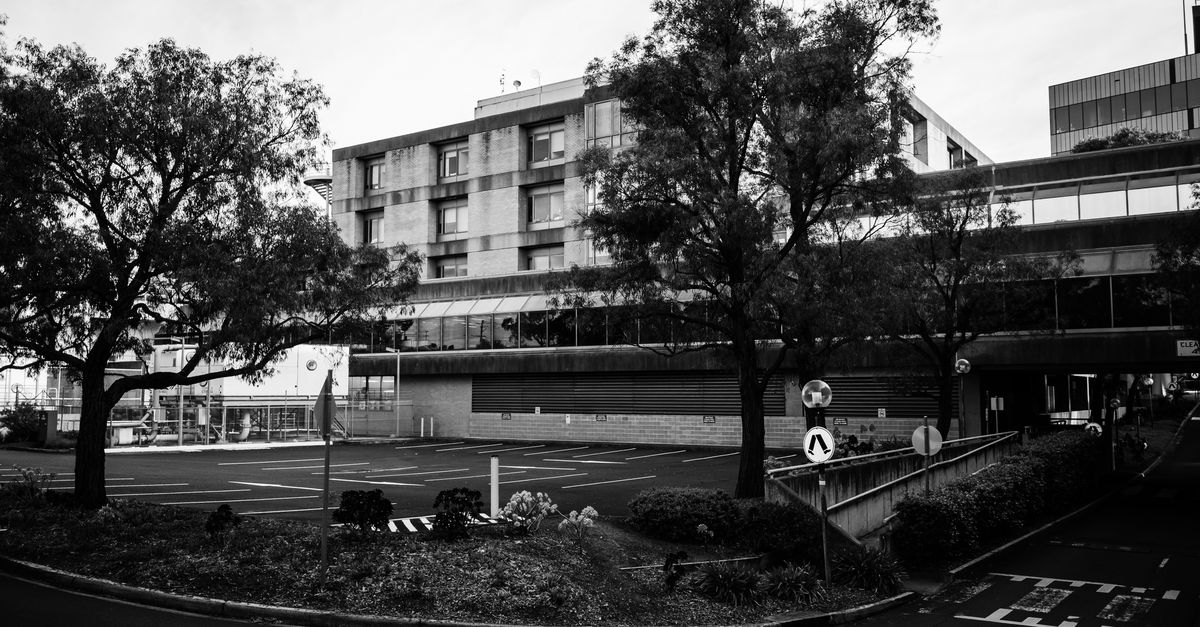 Black and white photo of a modern concrete building with adjacent trees and parking lot.