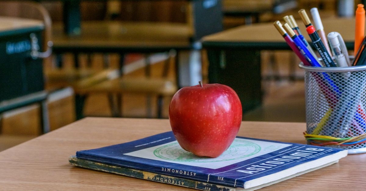 Red apple on books with stationery in a classroom, symbolizing education and knowledge.