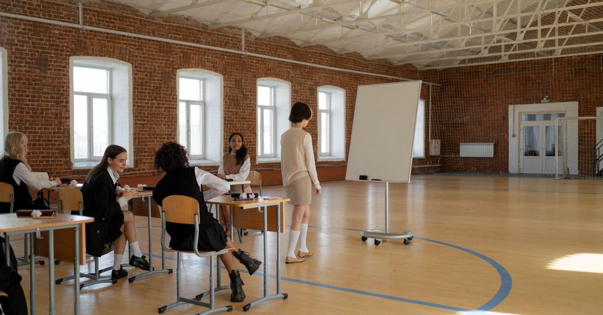 Students in school uniforms engaged in a lesson with a teacher in a spacious classroom.