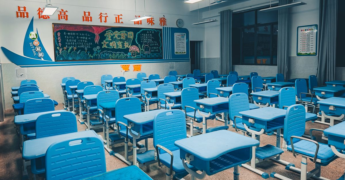 Spacious classroom with blue desks and vibrant decorated chalkboard, ready for students.