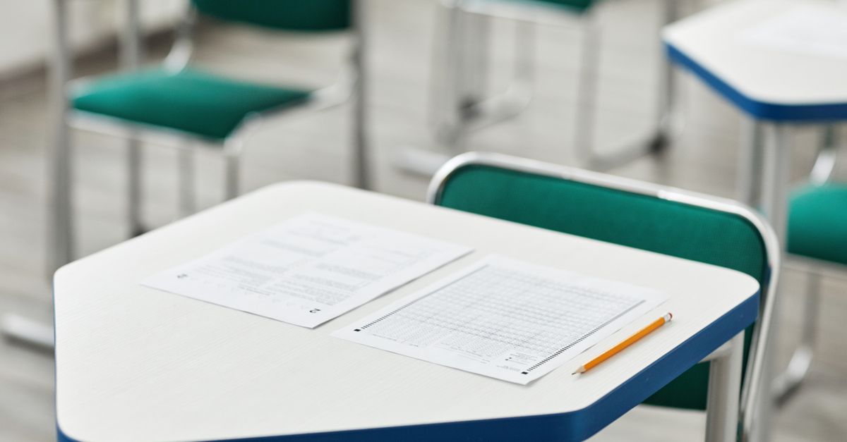 A close-up of an empty classroom desk with exam papers and a pencil, highlighting education and testing environment.