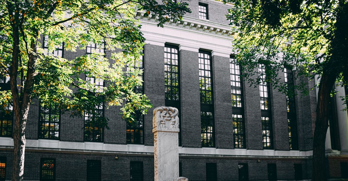 Exterior view of a university building with a stone statue and surrounding trees.