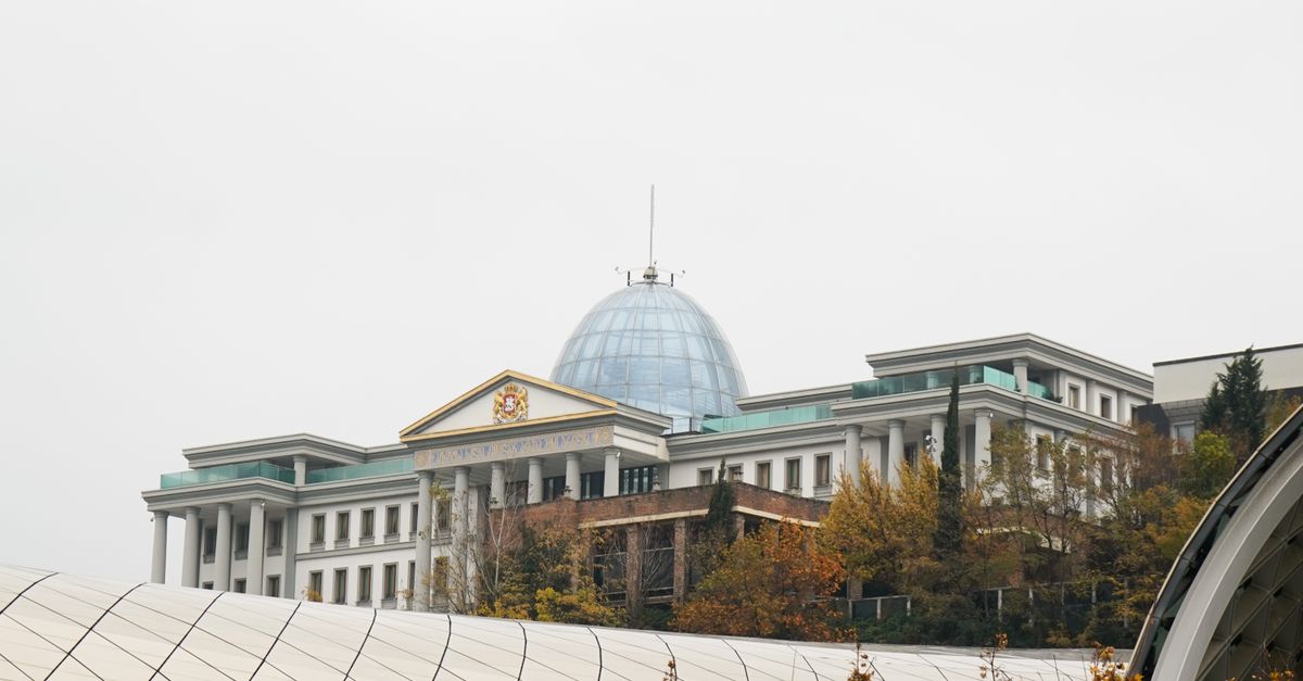 A modern palace with a dome surrounded by autumn trees under an overcast sky.